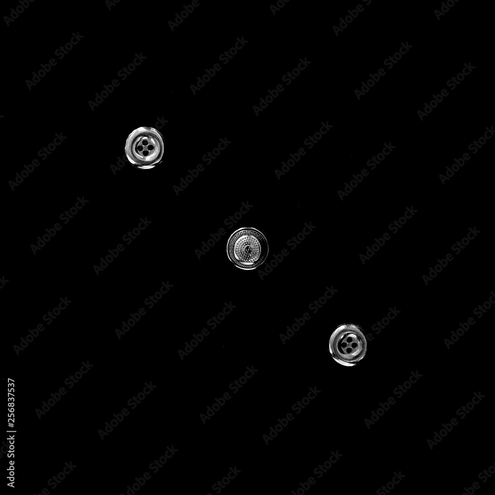Geometric composition on the diagonal of two buttons and a sewing thimble, all of steel, on a black background