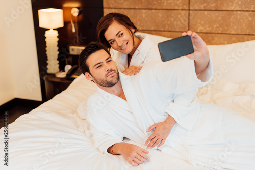 happy couple taking selfie on smartphone while lying on bed