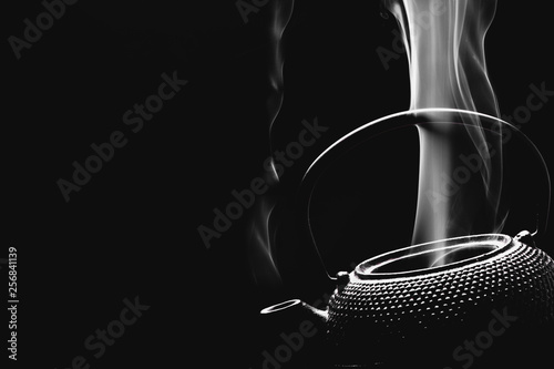 Tea kettle with boiling water. Steaming teapot on black background. Cooking concept.