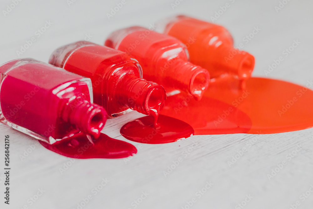 nail polish bottles in different shades of red to orange and purple spilling color on wooden surface nail polish bottles in different shades of red to orange and purple spilling color on wooden surface