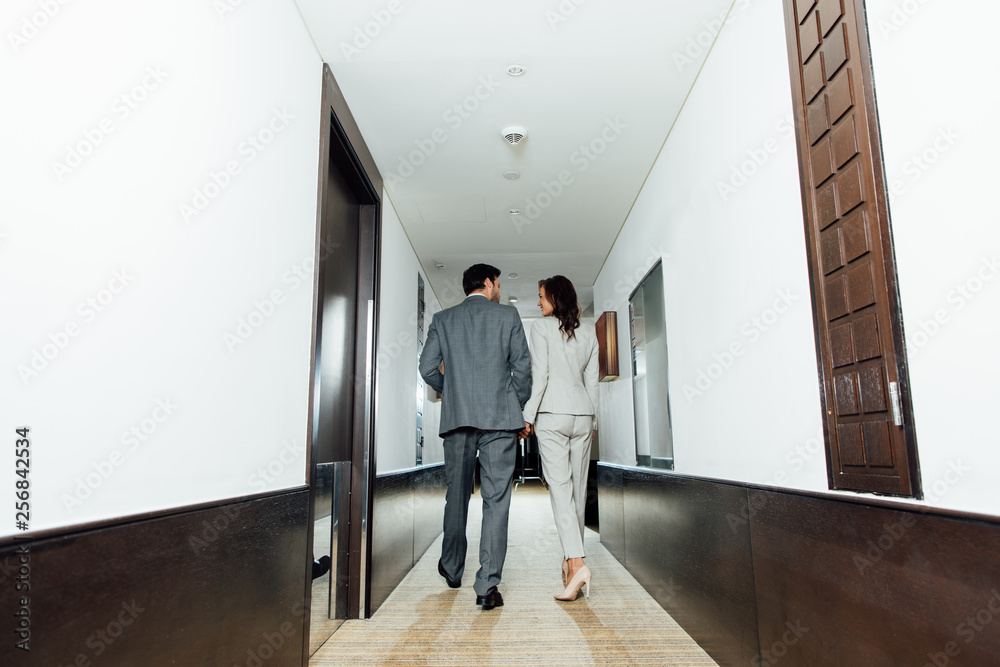 confident businessman businesswoman in formal wear holding hands and walking in hotel corridor