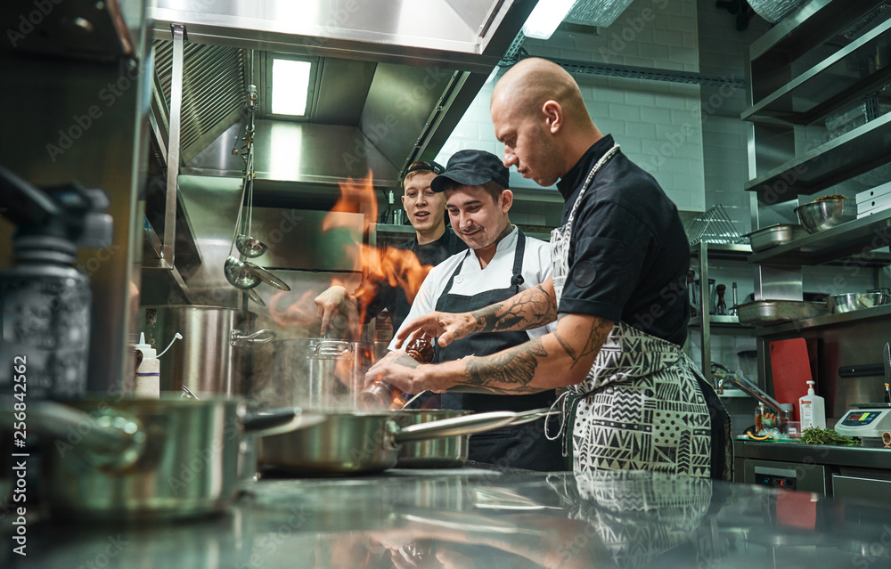 © Friends Stock - Extreme cooking. Profesional chef teaching his two young trainees how how to flambe food safely. Restaurant kitchen © Friends Stock - Extreme cooking. Profesional chef teaching his two young trainees how how to flambe food safely. Restaurant kitchen