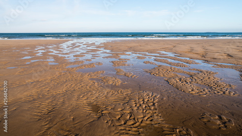 A tranquil scene of the beach at Bamburgh  Northumberland  with sand and a stream flowing towards the sea.