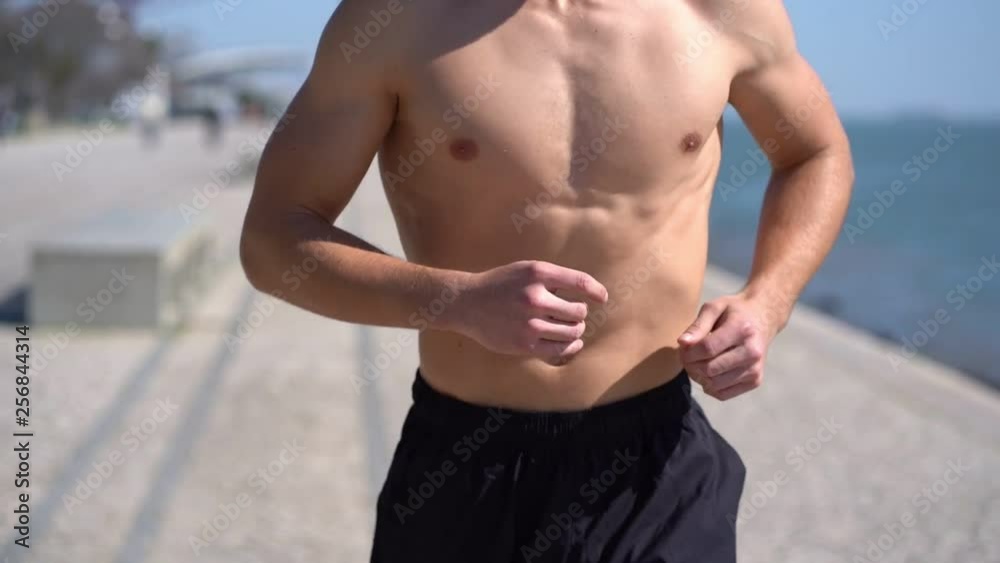 Cropped shot of shirtless sportsman running at riverside. Mid section of muscular barechested