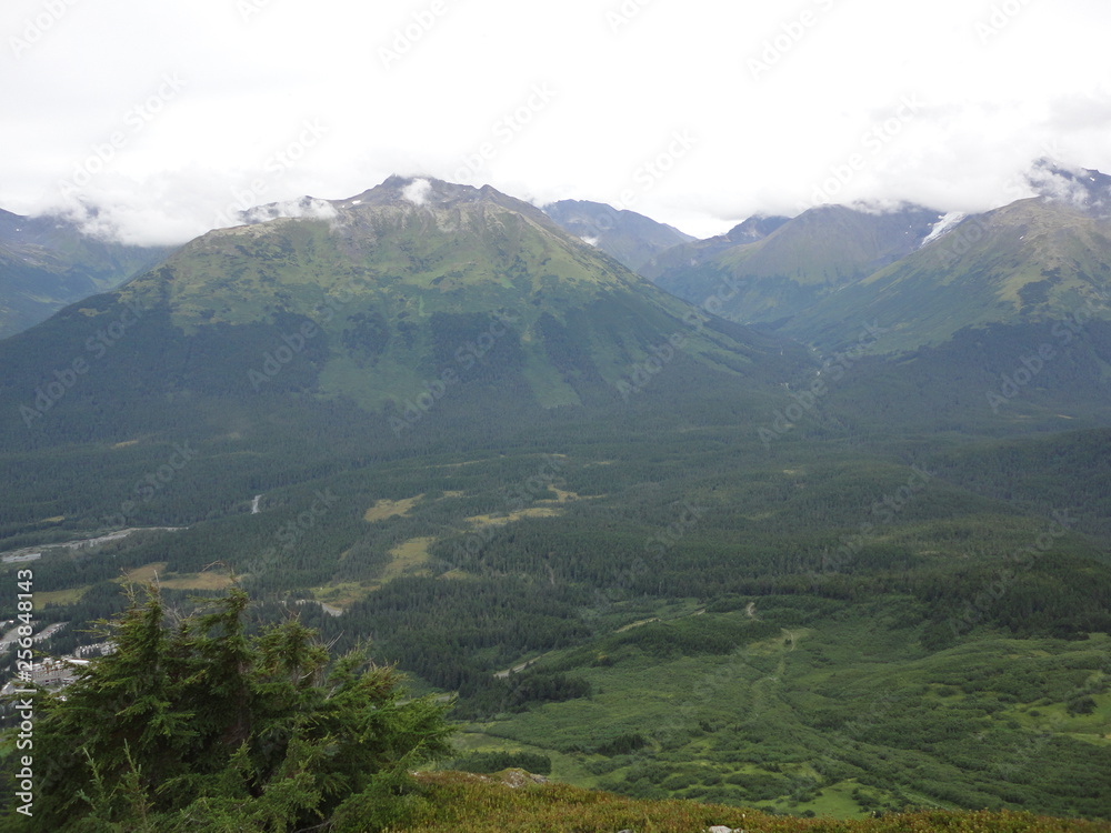 View from atop a mountain in the wilderness of Alaska. Peaks and ocean stretching off into the sky and clouds