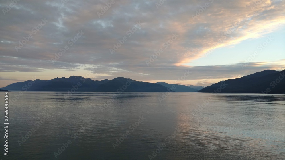 Sunset over the Pacific Ocean setting below a mountain range with bright colors gleaming off the clouds and ocean