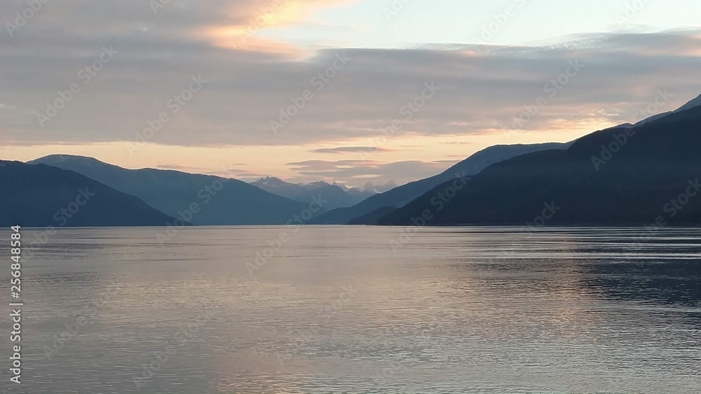 Obraz premium Sunset over the Pacific Ocean setting below a mountain range with bright colors gleaming off the clouds and ocean