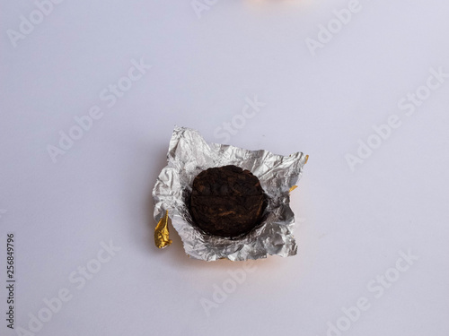 Mini tuocha pressed Pu'er tea from Chinese province Yunnan wrapped in golden foil on white background photo