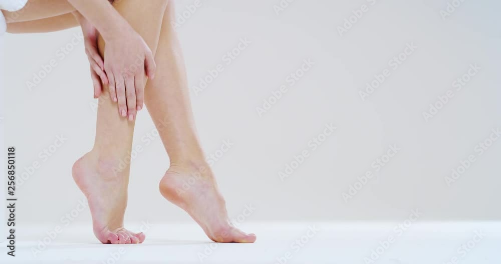 Slow motion close up of young woman touching her perfect hairless soft and silky legs after depilation isolated on a white background. Slow motion close up of young woman touching her perfect hairless soft and silky legs after depilation isolated on a white background.
