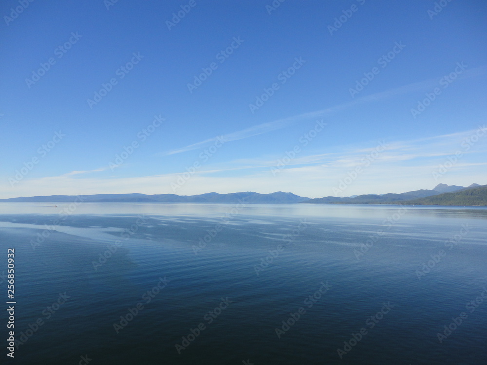 Calm Pacific Ocean in the inside passage in Alaska blue sky meets mountains and blue sea in a peacefully clear view Calm Pacific Ocean in the inside passage in Alaska blue sky meets mountains and blue sea in a peacefully clear view