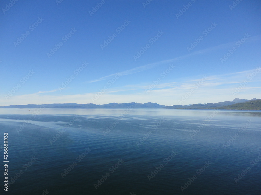 Calm Pacific Ocean in the inside passage in Alaska blue sky meets mountains and blue sea in a peacefully clear view