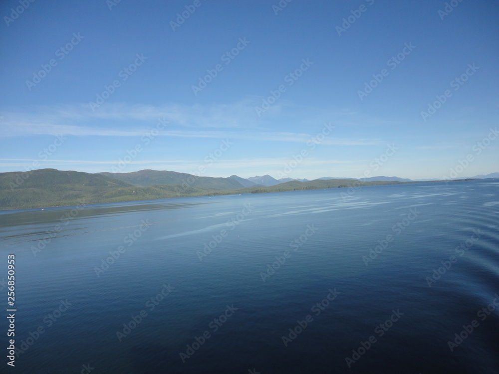 Calm Pacific Ocean in the inside passage in Alaska blue sky meets mountains and blue sea in a peacefully clear view