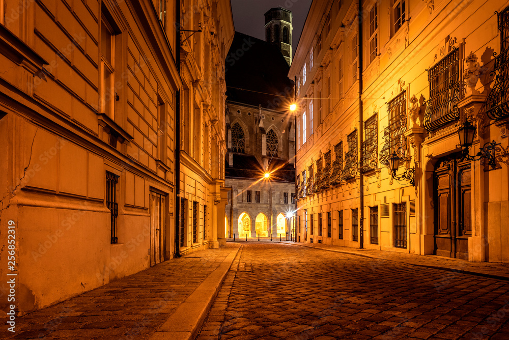 Austria, Vienna, Metastasiogasse:  Narrow alleyway street with cobblestone, old houses, lights and famous Minoriten church in the background at dark night in the city center of the Austrian capital.