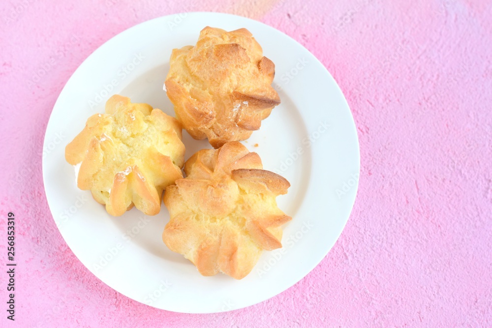 Delicious homemade gluten free eclairs on white plate on pink plaster textured table. Tasty french profiteroles filled traditional custard cream. Dish with gourmet pastries on pink backdrop 