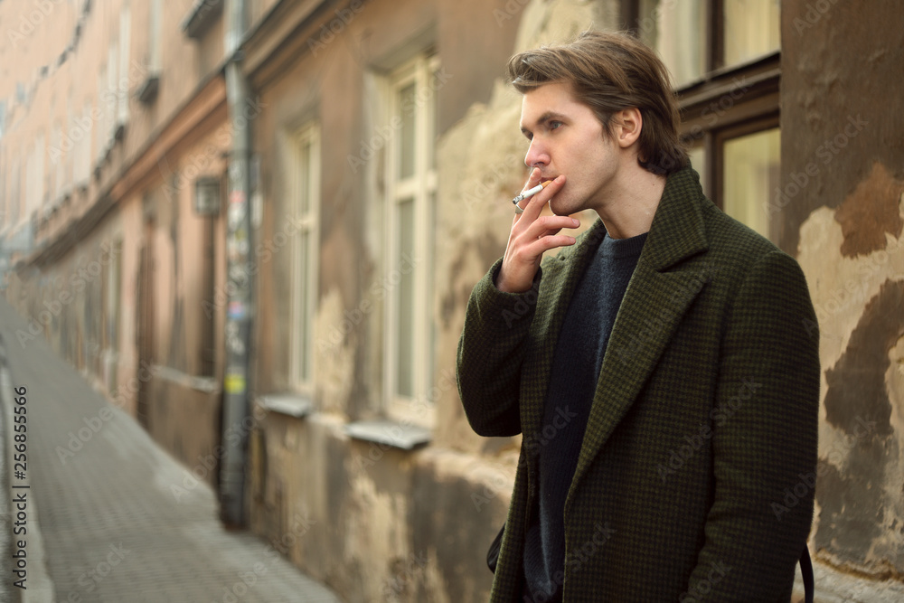 Man on the old street smoking cigarettes, in a long coat. Man befriends a cigarette in the city. A man like from old movies, vintage. Man on the old street smoking cigarettes, in a long coat. Man befriends a cigarette in the city. A man like from old movies, vintage.