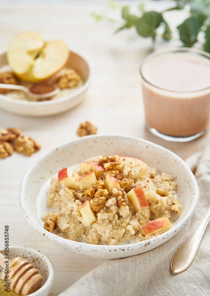 Oatmeal with apple, nuts, cinnamon, honey and cup of cocoa on white wooden light background. Vertical. Healthy diet breakfast Oatmeal with apple, nuts, cinnamon, honey and cup of cocoa on white wooden light background. Vertical. Healthy diet breakfast