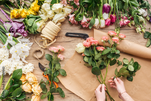 Partial view of florist making flower bouquet on wooden surface