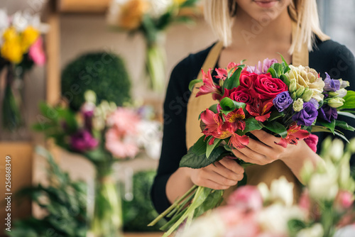 Cropped view of florist in apron holding bouquet in flower shop