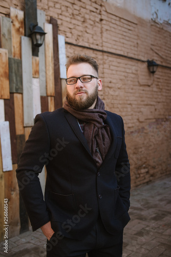 A man with a beard in a black warm coat with a scarf poses to advertise men's clothing in the winter. Advertise men's clothing