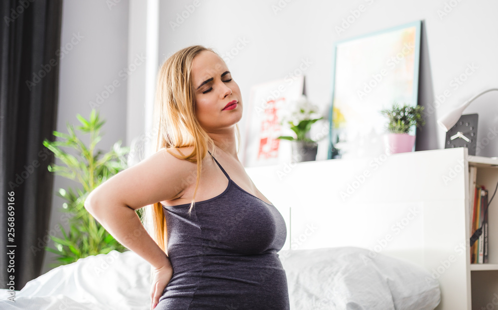 Lower back pain during pregnancy, pregnant woman sitting on bed at home Lower back pain during pregnancy, pregnant woman sitting on bed at home