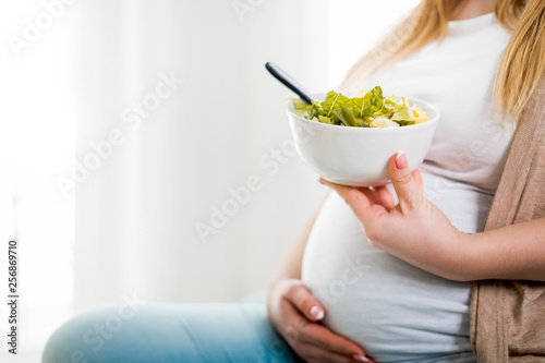 Happy pregnant woman at home eating vegetable salad at home