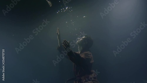 drowning man is stretching hands up to surface of sea, underwater shot