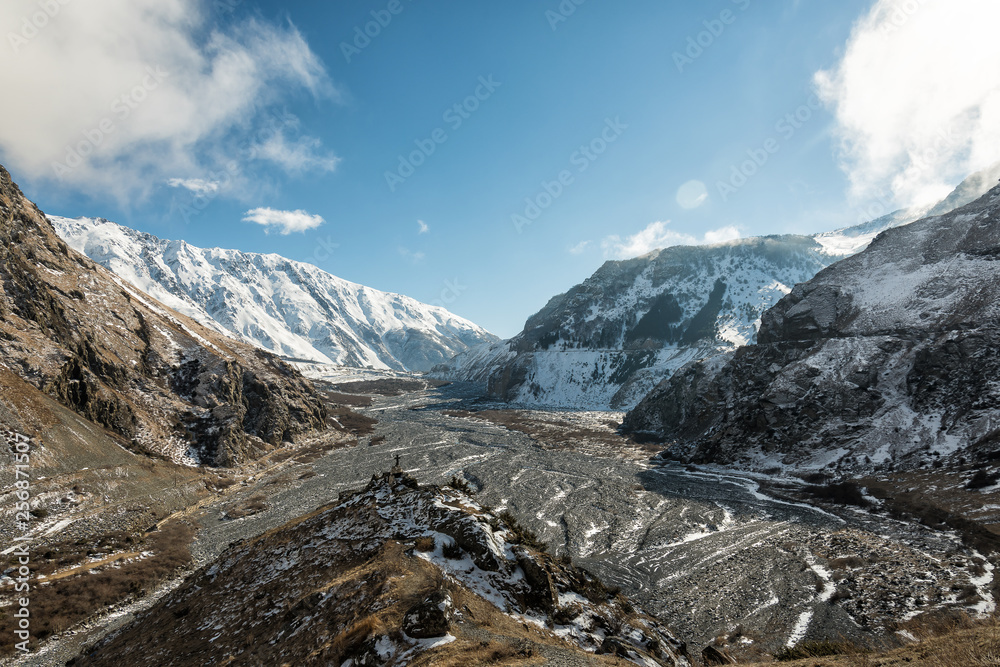 Riverbed in the valley among the snow-capped mountains. Blue sky on the background of snow-capped peaks and riverbed