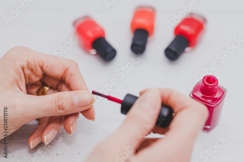 woman s hands with red nail polish bottle and other colors on wooden surface