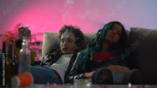 Couple of intoxicated young people sitting relaxed in messy room, night party