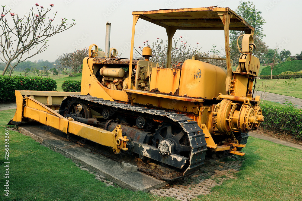Old yellow rusty crawler tractor in the field. Old crawler tractor on green garden Old yellow rusty crawler tractor in the field. Old crawler tractor on green garden