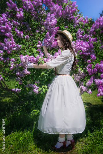 Girl in a white dress hugs a flowering lilac