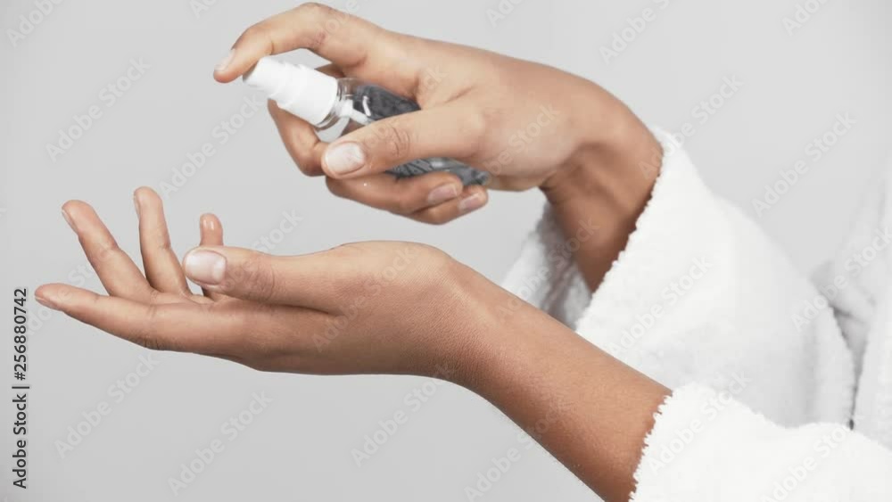 cropped view of african american girl holding antibacterial spray bottle and spraying on hand isolated on grey 