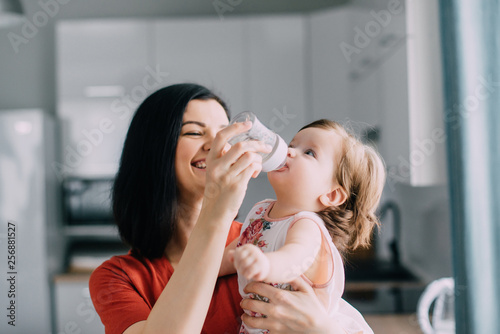 Young female feeds baby daughter in kitchen at home