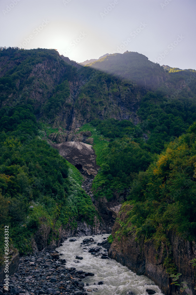 Caucasian Mountain River in the woods in the morning at dawn when the first rays of the sun make their way into the valley between the mountains in the surroundings of Dombai.
