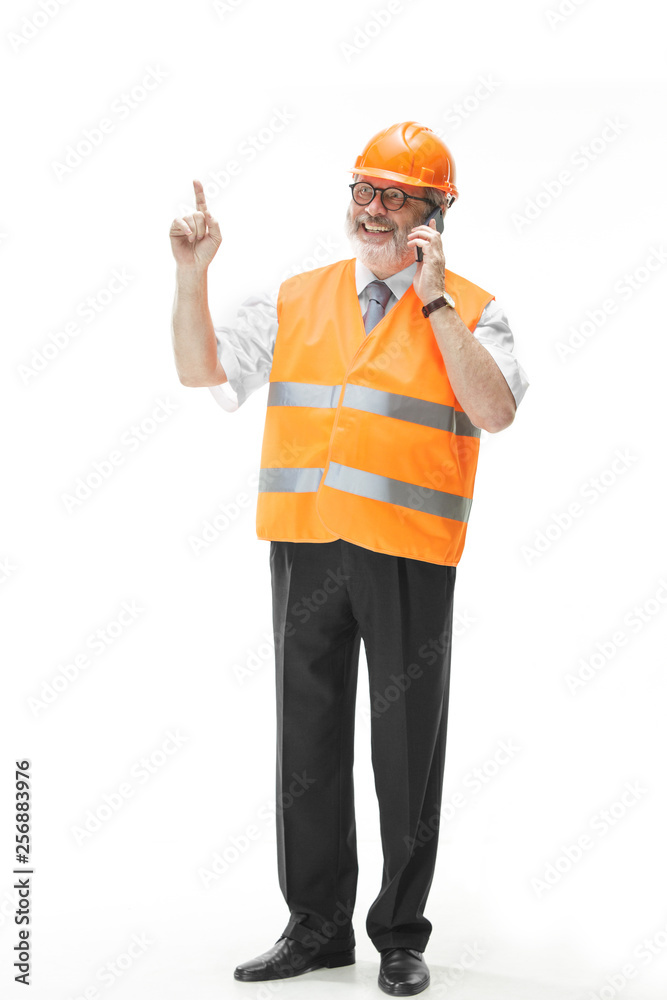The builder in a construction vest and an orange helmet talking on a mobile phone about something. Safety specialist, engineer, industry, architecture, manager, occupation, businessman, job concept The builder in a construction vest and an orange helmet talking on a mobile phone about something. Safety specialist, engineer, industry, architecture, manager, occupation, businessman, job concept