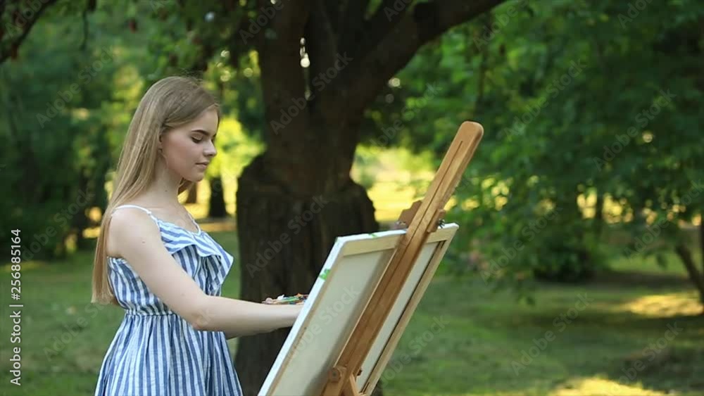 Beautiful girl draws a picture in the park using a palette with paints ...
