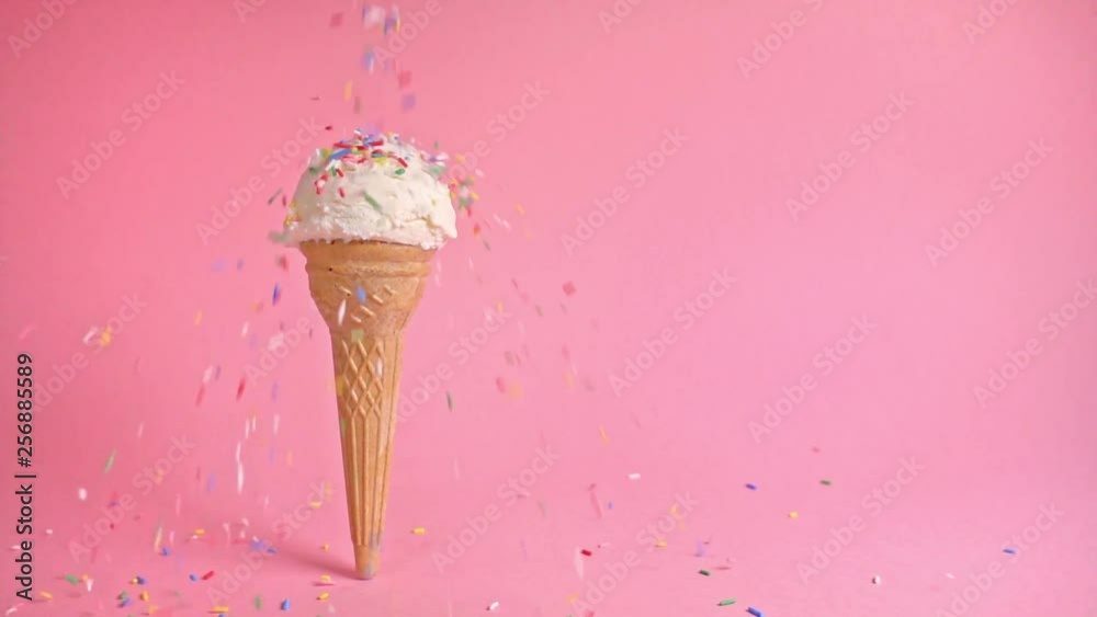 funny creative concept of wafer cone with ice cream covered and strewing sprinkles on pink background, copy space, slow motion