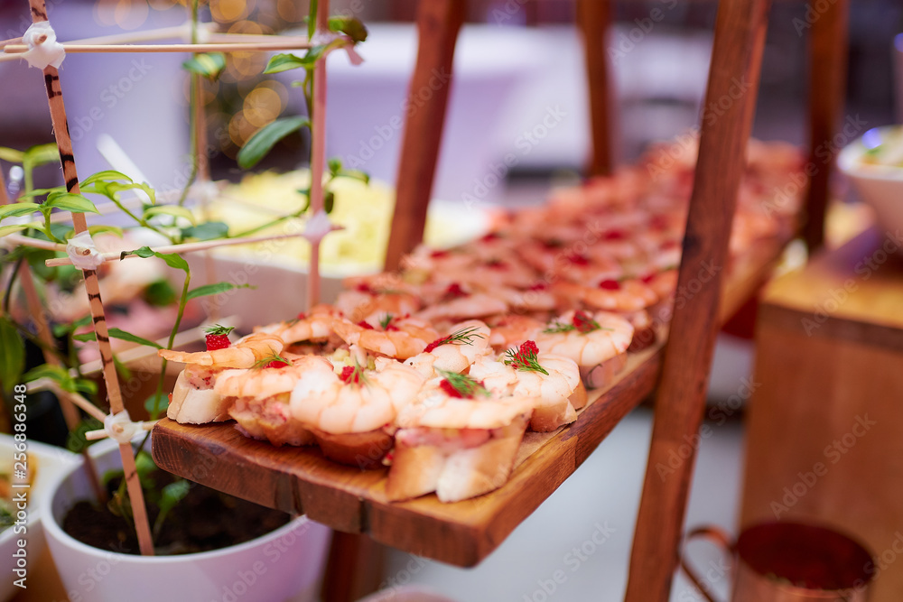 Tasty snacks on the wooden plate in a restaurant. Toasts with shrimps.  An amazing bokeh on the background.