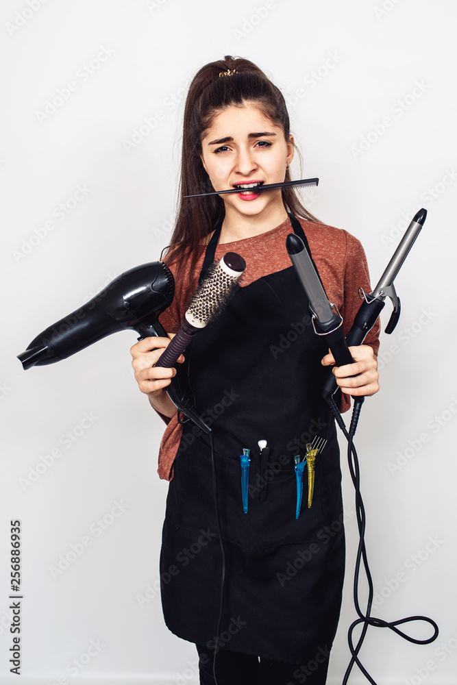 young girl hairdresser with a curling iron, hairdryer, comb in teeth. young girl hairdresser with a curling iron, hairdryer, comb in teeth.