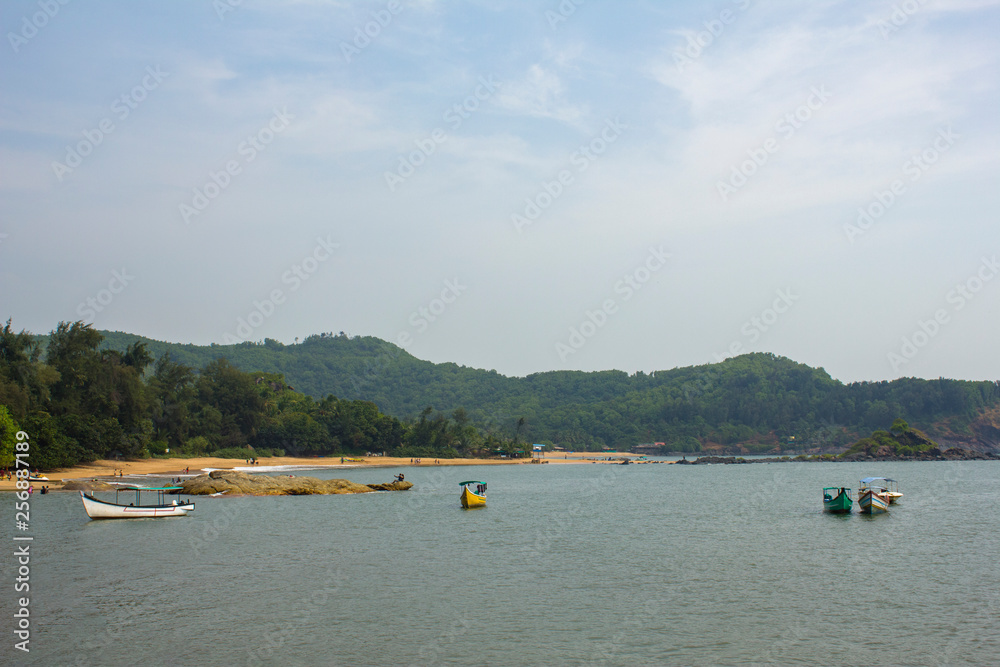 Fototapeta premium pleasure boats with tents on the sea near the shore against the background of a sandy beach and hills with a green forest, view from the ocean