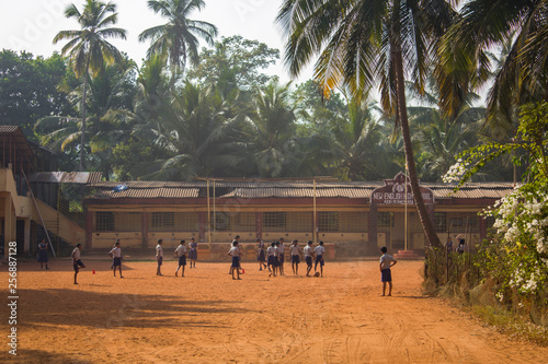 Querim, Goa/India - 10.01.2019: Indian schoolchildren boys and girls playing football barefoot in the school yard under green palm trees