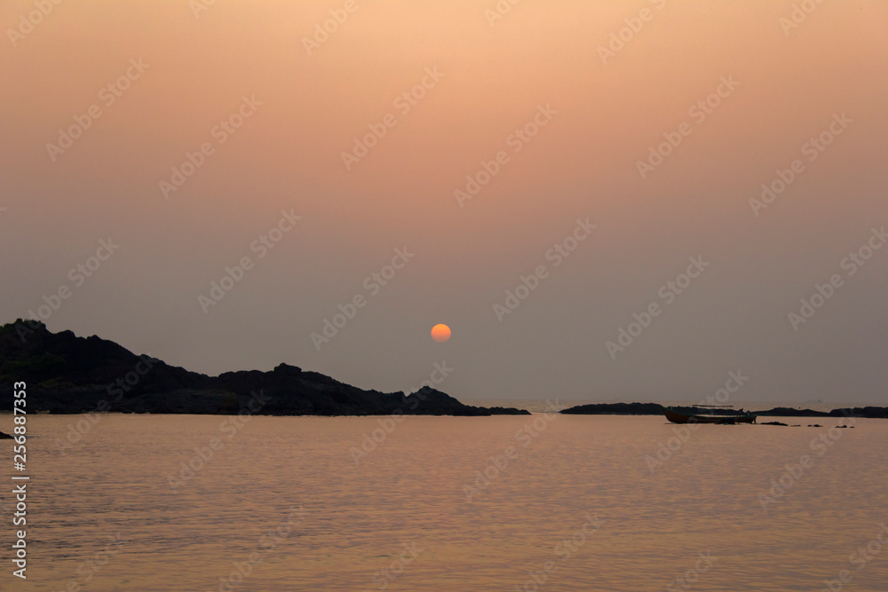 black silhouettes of rocks and the sun over the ocean in the evening, view from the sea