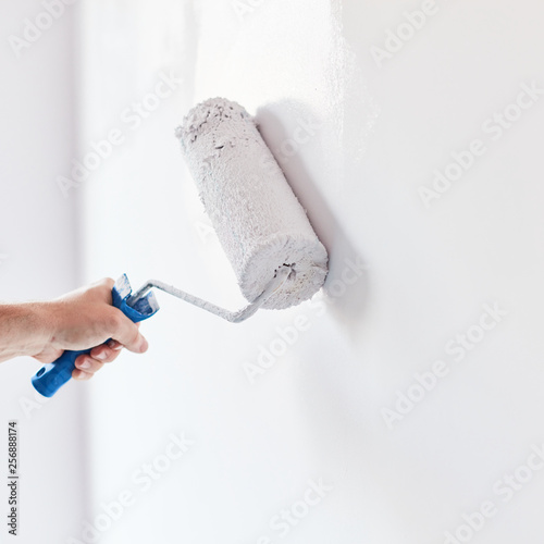 Fototapeta Naklejka Na Ścianę i Meble -  Male hand painting wall with paint roller. Painting apartment, renovating with white color paint