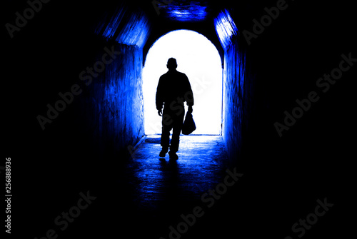 Person walking through tunnel towards light at end. Accomplishing goal or leaving darknenss for light.