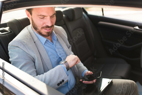 Attractive young modern businessman looking at watch while driving in the car to the work. Late to work, hurry to work. Successful businessman going to work.