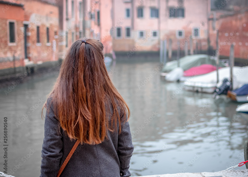 Venice / Italy 19 february 2019 : portrait of woman,she has long brown hair and she is wearing a grey coat and a multicolor scarf she looks the boats and the rives
