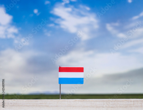 Flag of Luxembourg with vast meadow and blue sky behind it.