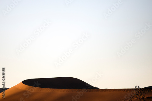 Three tourists walk over a sand dune in Sossuvlei, Namibia