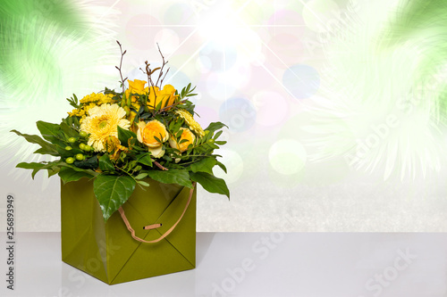 Fototapeta Naklejka Na Ścianę i Meble -  Close-up of a beautiful bouquet with yellow flowers in a decorative green gift box on a bright table over abstract spring landscape isolated on a white background. Macro. Space for design.