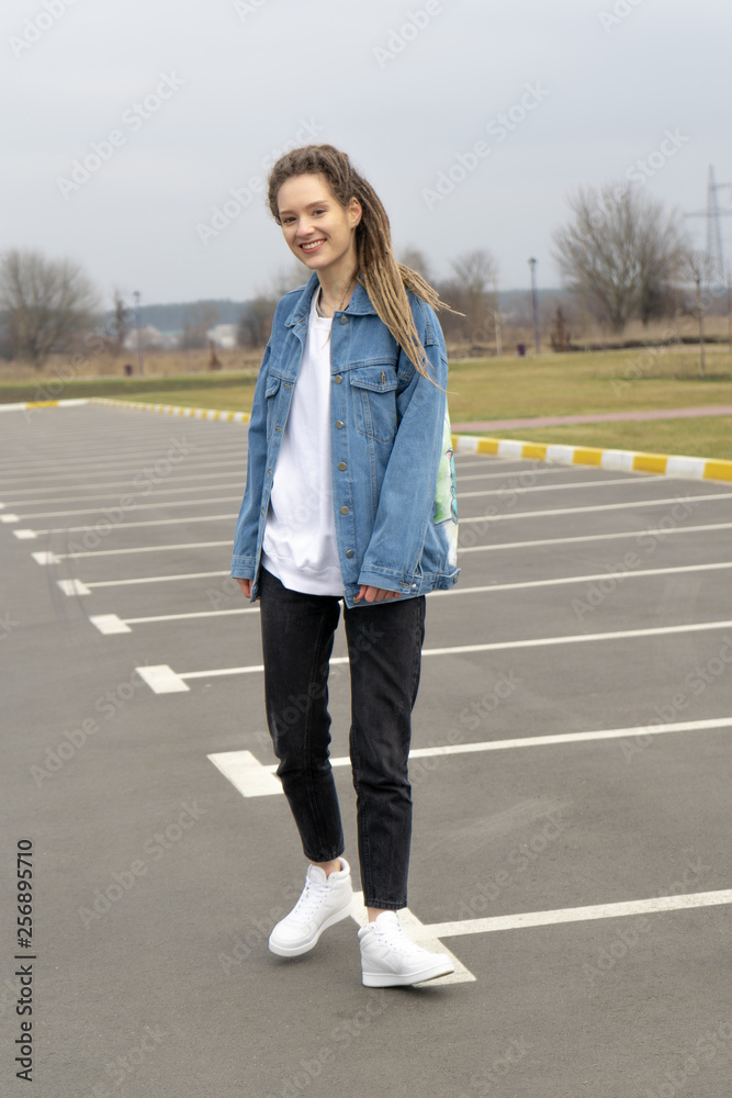 Young woman with dreadlocks in casual clothes walking on the parking in the early spring 